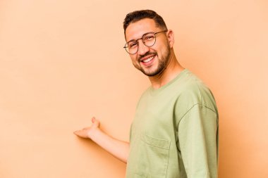 Latin kökenli genç bir adam bej arka planda izole edilmiş hoş bir ifade sergiliyor..