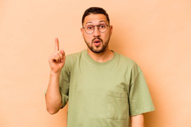 Latin kökenli genç adam bej arka planda izole edilmiş. Ağzı açık, üst tarafı işaret ediyor..