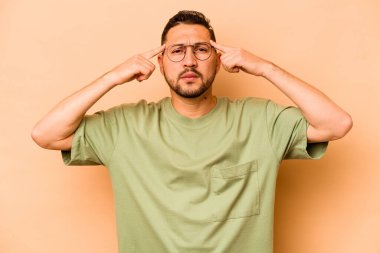 Latin kökenli genç bir adam bej arka planda izole edilmiş bir vazifeye odaklanmış, işaret parmaklarını işaret ediyor..