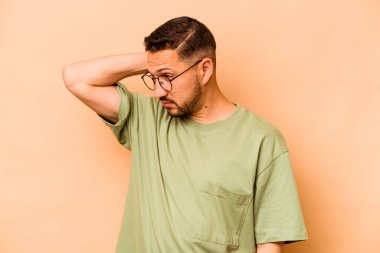 Latin kökenli genç adam bej arka planda izole edilmiş. Çok yorgun ve uykulu. Elini başının üstünde tutuyor..