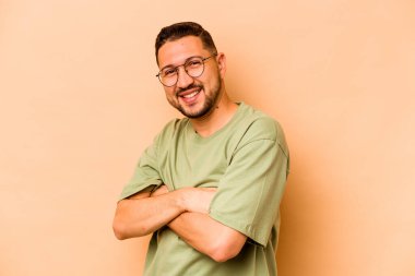 Bej arka planda izole edilmiş genç İspanyol bir adam. Kendini güvende hissediyor, kararlılıkla kollarını kavuşturuyor..