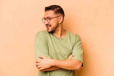 Genç İspanyol adam bej arka planda izole edilmiş gülüyor ve eğleniyor..