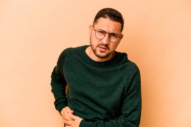Latin kökenli genç bir adam bej arka planda karaciğer ağrısı ve karın ağrısı çekiyor..