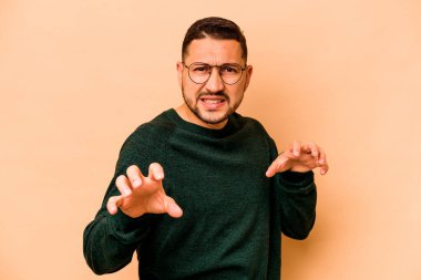 Latin kökenli genç bir adam bej arka planda izole edilmiş. Pençeleri kedi taklidi yapıyor. Saldırgan bir hareket..