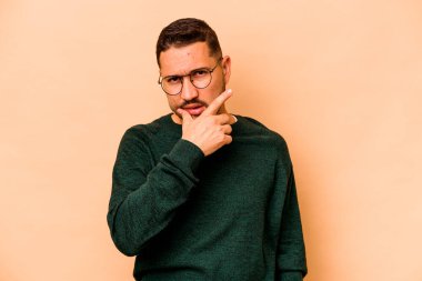 Latin kökenli genç bir adam bej arka planda izole edilmiş. Bir strateji planlıyor, bir iş yolu düşünüyor..