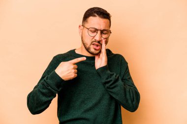 Genç İspanyol adam bej arka planda izole edilmiş güçlü bir diş ağrısı, azıdişi ağrısı var..