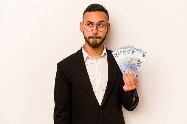 Genç İspanyol iş adamının elinde banknotlar var. Beyaz arka planda izole edilmiş. Kafası karışık ve kararsız..