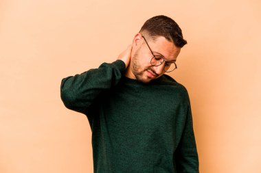 Latin kökenli genç bir adam bej arka planda izole edilmiş. Stres yüzünden boynu ağrıyor, masaj yapıyor ve elle dokunuyor..