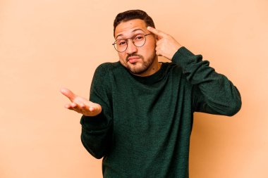 Latin kökenli genç bir adam bej arka planda izole edilmiş ve elinde bir ürün tutuyor..