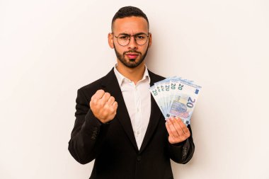 Beyaz arka planda izole edilmiş banknotlar tutan genç bir İspanyol iş adamı yumruğunu kameraya gösteriyor, agresif yüz ifadesi var..