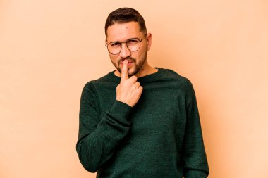 Latin kökenli genç adam bej arka planda izole edilmiş düşünüyor ve yukarı bakıyor, yansıtıyor, düşünüyor, bir fantezi kuruyor..