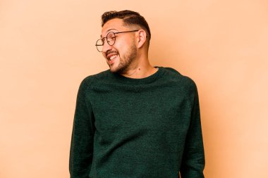Latin kökenli genç adam bej arka planda izole edilmiş. Gülüyor ve gözlerini kapatıyor. Rahatlamış ve mutlu hissediyor..