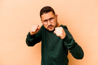 Latin kökenli genç bir adam bej arka planda izole edilmiş. Yumruk atıyor, sinirleniyor, tartışıyor, boks yapıyor..