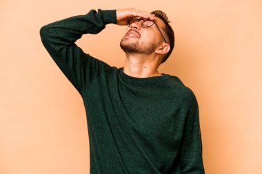 Latin kökenli genç bir adam bej arka planda yalnızken mutlu bir şekilde ellerini başının üstünde tutuyor. Mutluluk kavramı.