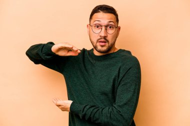 Latin kökenli genç adam bej arka planda iki eliyle bir şey tutuyor, ürün sunumu..