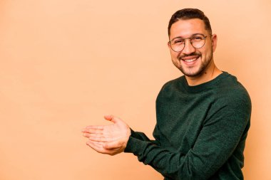 Latin kökenli genç adam bej arka planda izole edilmiş. Elinde palmiye ağacında bir kopyası var..