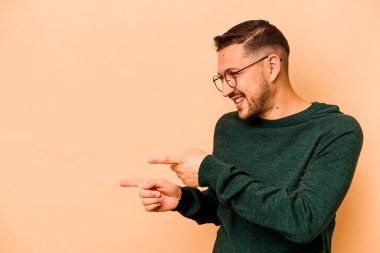 Latin kökenli genç adam bej arka planda izole edilmiş, başparmak uzakta, gülüyor ve kaygısız..