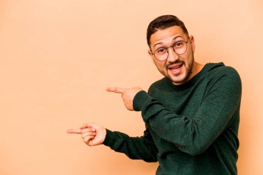 Latin kökenli genç adam bej arka planda izole edilmiş. İşaret parmaklarıyla işaret ettiği için heyecanlı..