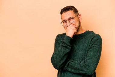 Latin kökenli genç adam bej arka planda izole edilmiş gülerek, kaygısız, doğal duygularla gülüyor..