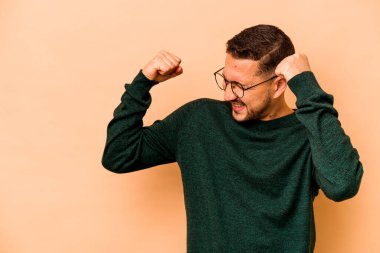 Latin kökenli genç adam bej arka planda izole edilmiş zafer kazandıktan sonra yumruğunu kaldırıyor, kazanan konsept.