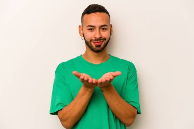 Beyaz arka planda izole edilmiş genç İspanyol bir adam avuçlarıyla bir şey tutuyor ve kameraya sunuyor..