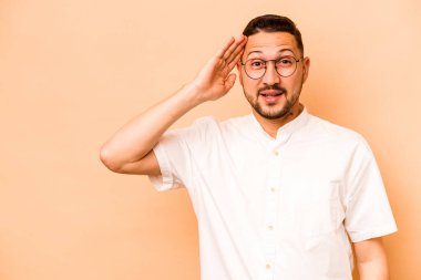 Latin kökenli genç adam bej arka planda izole edilmiş yüksek sesle bağırıyor, gözleri açık ve elleri gergin tutuyor.