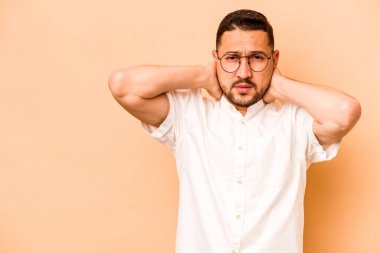 Latin kökenli genç adam bej arka planda izole edilmiş kafasının arkasına dokunuyor, düşünüyor ve bir seçim yapıyor..