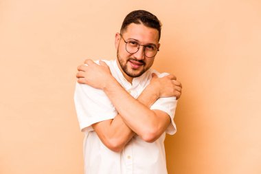 Latin kökenli genç adam bej sarılıp, kaygısız ve mutlu bir şekilde sırıtıyor..