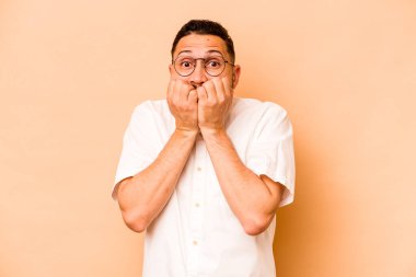 Latin kökenli genç bir adam bej arka planda izole edilmiş tırnak yiyor, gergin ve çok endişeli..