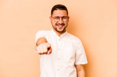 Latin kökenli genç adam, bej arka planda izole edilmiş. Önü gösteren neşeli gülümsemeler..