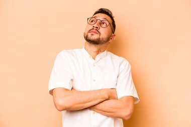 Latin kökenli genç adam bej arka planda izole edilmiş hedeflerine ve amaçlarına ulaşma hayali kuruyor.