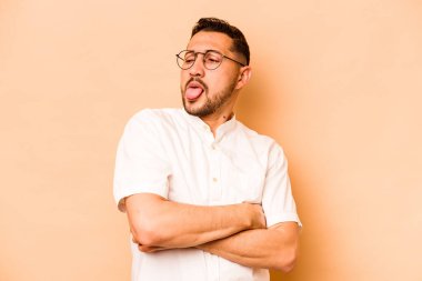 Latin kökenli genç adam, bej arka planda izole edilmiş komik ve dost canlısı bir dil kullanıyor..