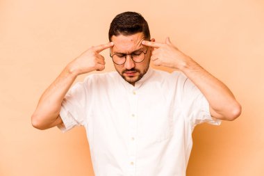 Latin kökenli genç bir adam bej arka planda izole edilmiş bir vazifeye odaklanmış, işaret parmaklarını işaret ediyor..