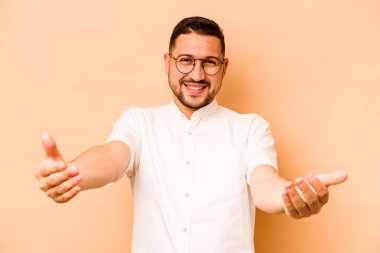 Latin kökenli genç bir adam bej arka planda izole edilmiş hoş bir ifade sergiliyor..