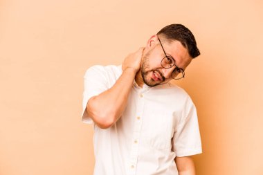 Latin kökenli genç bir adam bej arka planda izole edilmiş. Oturaklı yaşam tarzından dolayı boyun ağrısı çekiyor..