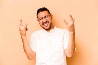 Latin kökenli genç adam bej arka planda izole edilmiş boynuzları devrim konsepti olarak gösteriyor..
