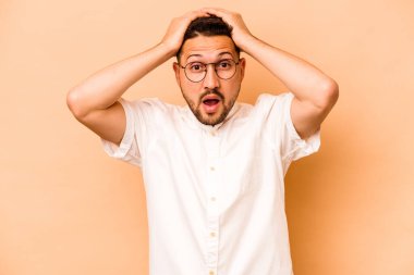 Latin kökenli genç adam bej arka planda izole edilmiş şaşırmış ve şok olmuş..
