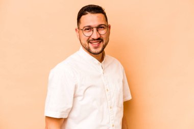 Latin kökenli genç adam bej arka planda izole edilmiş. Kendine güveniyor. Kalçaları tutuyor..