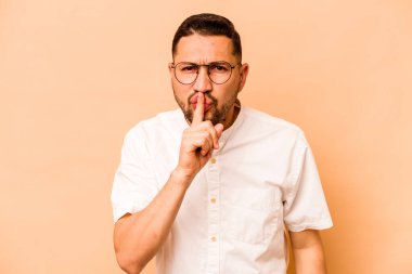 Latin kökenli genç bir adam bej arka planda izole edilmiş bir şekilde sır saklıyor ya da sessizlik istiyor..