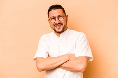 Bej arka planda izole edilmiş genç İspanyol bir adam. Kendini güvende hissediyor, kararlılıkla kollarını kavuşturuyor..