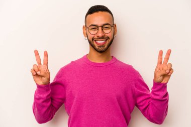 Beyaz arka planda izole edilmiş genç İspanyol adam zafer işareti gösteriyor ve gülümsüyor..