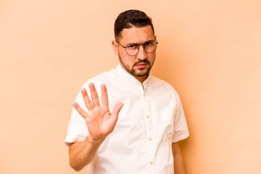 Latin kökenli genç bir adam, bej arka planda izole edilmiş, tiksinti belirtisi gösteren birini reddediyor..