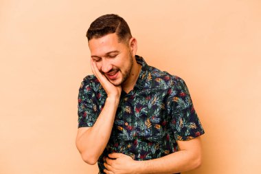 Latin kökenli genç adam bej arka planda izole edilmiş mutlu bir şekilde gülüyor ve elleri karnında gezdirirken eğleniyor..