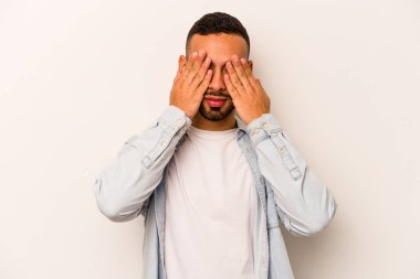 Beyaz arka planda izole edilmiş genç İspanyol adam elleriyle gözlerini kapatmaktan korkuyor..