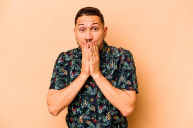 Latin kökenli genç adam bej arka planda izole edilmiş. Ağzı elleri endişeli görünüyor..