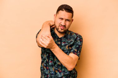 Latin kökenli genç bir adam bej arka planda izole edilmiş. Stres yüzünden boynu ağrıyor, masaj yapıyor ve elle dokunuyor..