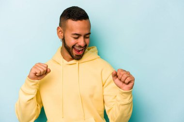 Genç İspanyol adam mavi arka planda izole edilmiş dans ediyor ve eğleniyor.