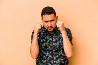 Latin kökenli genç bir adam bej arka planda izole edilmiş. Yumruk atıyor, sinirleniyor, tartışıyor, boks yapıyor..