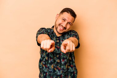 Latin kökenli genç adam bej arka planda izole edilmiş. Parmaklarıyla öne bakıyor..