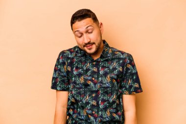 Latin kökenli genç adam bej arka planda izole edilmiş. Gülüyor ve gözlerini kapatıyor. Rahatlamış ve mutlu hissediyor..